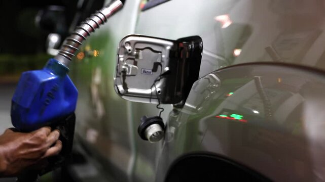 Pickup truck stops at a fuel station at night : Male worker's hand slowly takes out the fuel nozzle from the fuel filler port into the diesel fuel tank of a pickup truck.