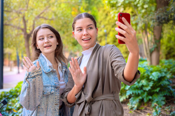 Happy female friends taking a self portrait with cell phone and smiling outdoors
