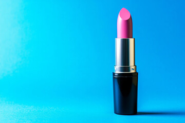 Obraz premium A bright pink lipstick stands upright against a vibrant blue background, emphasizing beauty and cosmetic appeal.