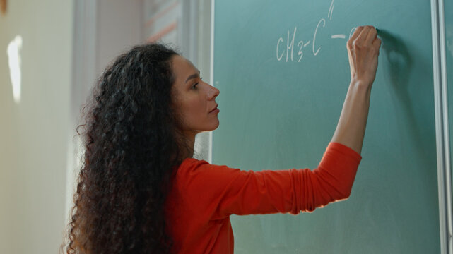 Caucasian girl student Hispanic woman Latina American female in university college auditorium writing chalk mathematical calculations formula on board black board in classroom study education school