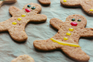 Gingerbread man cookies on baking tray. Decorated cookie with smile and eyes. Christmas cookies background. Homemade biscuits. Cinnamon cookies on baking paper. Funny ginger men biscuits.