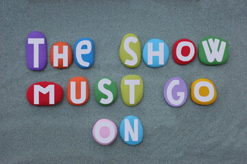 The show must go on, creative text for a famous quote composed with hand painted multi colored stone letters over green sand