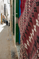 Tripoli, Libya, 4 November 2009.  A quiet street in the old city of Tripoli, Libya, with a rug hanging on the side of the wall and pedestrians in the background.