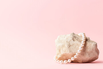 A string of white pearls placed on a rough beige stone, set against a soft pink background, creating a minimal and elegant composition.