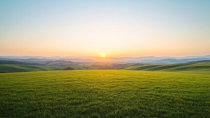Obraz premium A serene sunset over rolling green hills, with a golden glow illuminating the landscape.