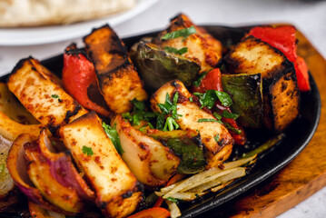 A sizzling platter of colorful vegetable skewers, grilled to perfection, sits atop a wooden board. Accompanying the dish is soft naan bread.
