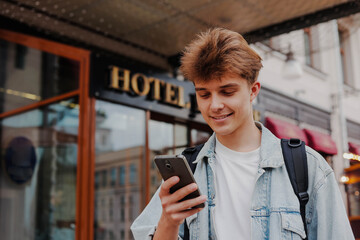 Young man tourist using his smartphone standing outside hotel