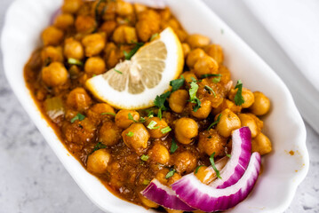 Traditional chickpea dish served in an elegant white dish. The dish is garnished with a lemon slice, red onion rings, and fresh herbs, hinting at vibrant flavors.