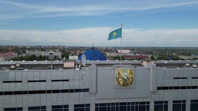

Kostanay, Kazakhstan - 06.04.2024 : The building of the city administration with the flag and coat of arms of Kazakhstan. The view from the drone.