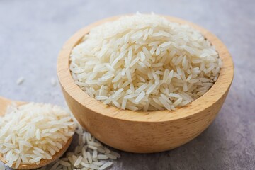 Uncooked white rice in wooden bowl on grey background, thai jasmice rice, thai fragrant rice