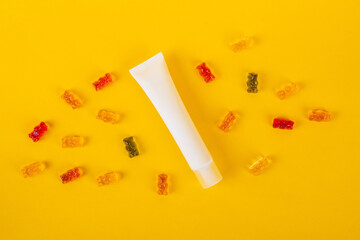 Cosmetic product in tube, bottle, lotion or serum and colorful candies, jelly on yellow background. 