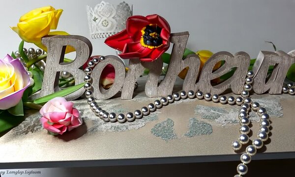 Sculpture en bois gris du mot fran&ccedil;ais "bonheur" entour&eacute;e de fleurs, collier de perles et bougies, ambiance douce, romantique et chaleureuse