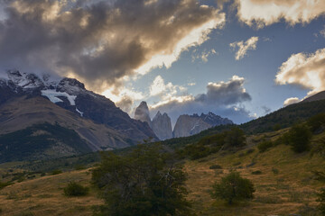 Torres del Paine in Patagonia, Chile, with its jagged granite peaks rising above the forested landscape, shrouded in dramatic clouds and mist.