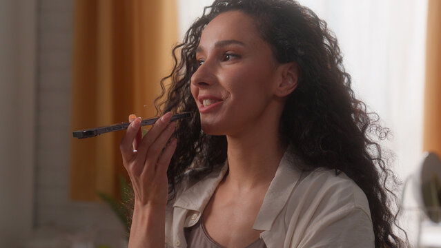 Happy smiling Hispanic woman girl Latina female lady homeowner householder at home kitchen record audio message speak mobile phone microphone dictate speech smartphone talk translate voice command app