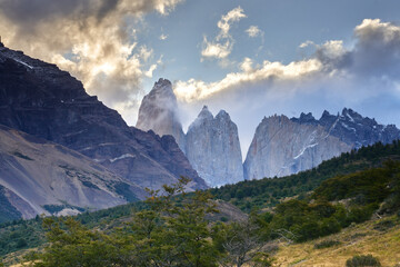 Torres del Paine in Patagonia, Chile, with its jagged granite peaks rising above the forested landscape, shrouded in dramatic clouds and mist.