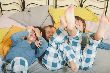 Three children are playing on a bed with blue and white plaid pajamas