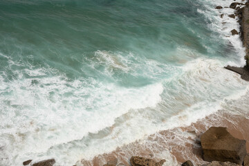 The waves crash against the shore creating a beautiful contrast of white foam and turquoise water