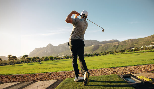 Wide shot of a male golfer on a panoramic golf course hitting a shot with scenic mountain background