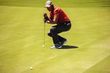 Obraz premium Focused golfer aiming carefully while leaning on putter to line up a crucial shot on the green