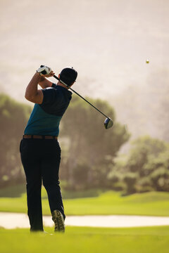 Man in close-up shot following through with golf swing on sunny course, featuring golf club and ball in mid-air