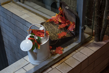 A white watering can next to an open suitcase full of hay. Autumn decoration