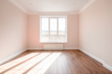 A spacious empty room featuring soft pink walls, wooden flooring, and sunlight streaming through the window