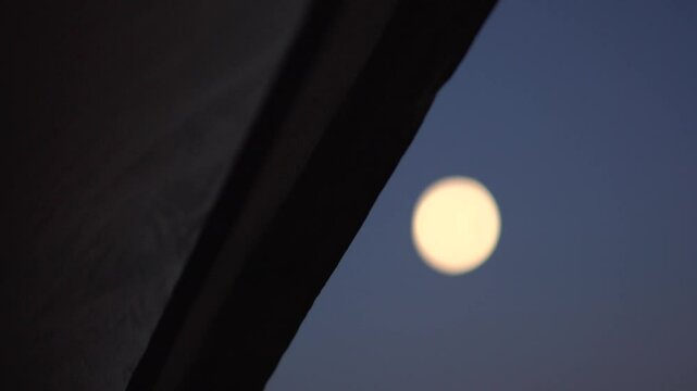 Dark tent door zip flapping in the wind with out of focus moon in the night sky
