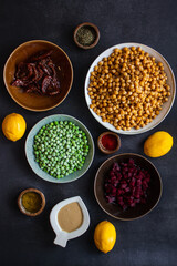 Ingredients for making hummus with peas, beets, sun-dried tomatoes are laid out individually on a dark background, top view.