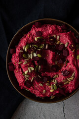 Plate with colorful pink hummus with beetroot flavor, seeds and beetroot pieces on dark background top view close up