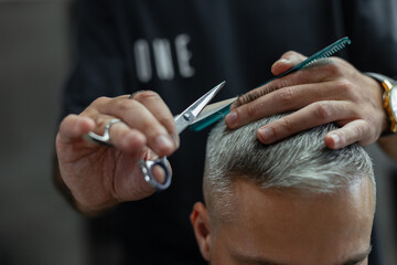 Man professional barber cuts gray hair guy with scissors and comb