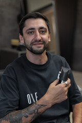 Male professional hairdresser with hair clipper sitting in chair in barber shop