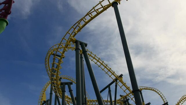 A yellow roller coaster twists and loops against a blue sky, with riders speeding through an inverted turn. A thrilling amusement park ride