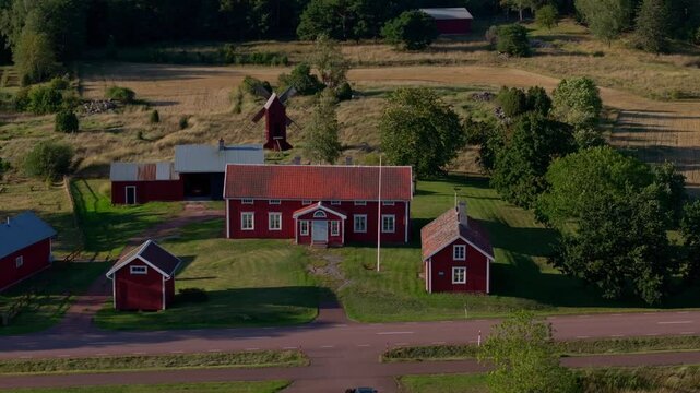 Aerial view of traditional red farm buildings in the rural countryside of Aland, Finland. A windmill stands tall on a sunny summer day