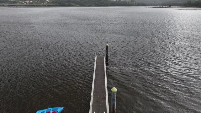 Pantalan con un barco amarrado azul en mitad de una ria