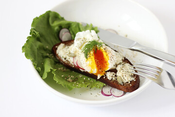 Eating Breakfast. Poached Egg on Rye Bread Toast with Cream Cheese, Seasoning with Pepper, Seeds, Salad Leaves and Radish. 