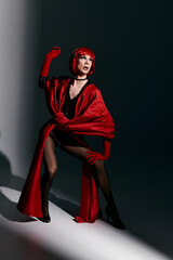 A young drag queen poses dramatically in striking red attire.