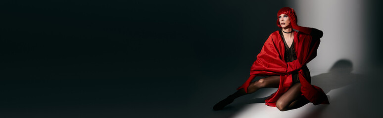 An attractive young drag queen showcases a stunning red outfit while posing expressively.