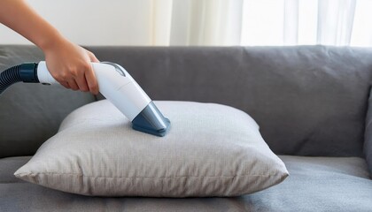 Person cleaning a pillow with a handheld vacuum cleaner.