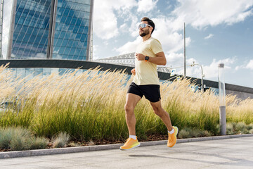 A Man Jogging in a Sunny Urban Setting Near Modern Architecture With Tall Grass Landscaping in the...