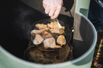 Enjoy the delightful experience of cooking chicken over a campfire using a trusty cast iron skillet during your outdoor culinary adventures