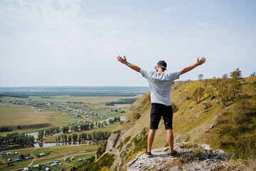 A man is confidently standing at the very top of a majestic mountain, his arms outstretched wide, embracing the vastness of nature around him with pure joy and excitement