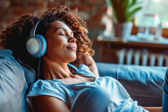 A woman sits on a couch and relaxes with headphones while listening to music.