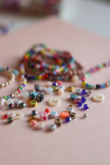 Colorful DIY necklaces, friendship bracelets and various plastic beads on pastel pink background. Selective focus.