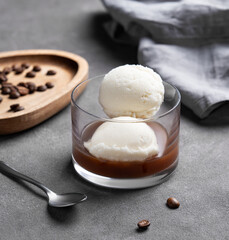 Affogato coffee with vanilla ice cream scoops and espresso in a glass on a dark background with coffee beans and spoon close up.