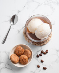 Affogato coffee with vanilla ice cream scoops and  espresso in a glass on a marble background with coffee beans and cookies.