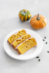 Slices of pumpkin sweet bread or cake with icing on a plate on a light background with decorative pumpkins and seeds.