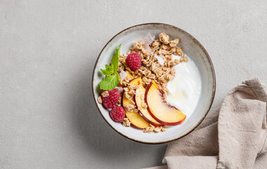 Greek natural yogurt with oat granola or muesli, peach, raspberry and mint in a bowl on a light background with napkin close up.