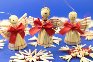 Handcrafted straw angels adorned with red bows, set against a blue background. Winter holiday decorations, DIY, traditional folk craft.