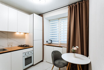 This modern kitchen is cozy, featuring stylish decor and abundant natural light pouring in through lovely curtains and contemporary design