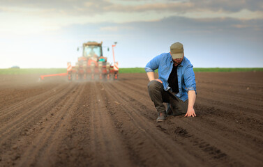 Farmer examing dirt while tractor is sowing field